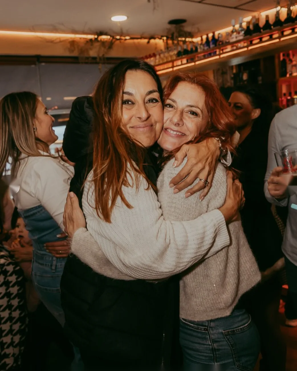 Dos amigas abrazándose junto a la barra iluminada de Café Tarifa en Mairena del Aljarafe
